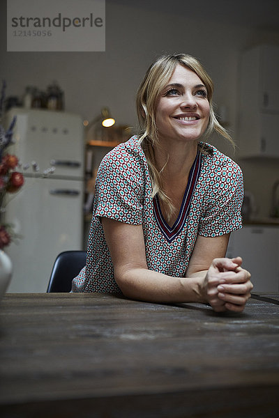 Porträt einer glücklichen Frau  die sich auf den Küchentisch lehnt.