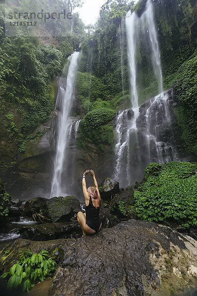 Indonesien  Bali  junge Frau am Wasserfall kauernd