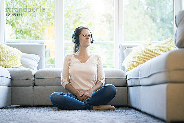 Frau sitzt allein auf der Couch und hört Musik mit Kopfhörern.