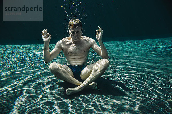 Mann sitzt in Yoga-Pose unter Wasser in einem Schwimmbad