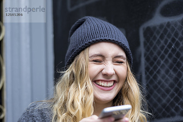 Porträt einer lachenden jungen Frau mit Smartphone
