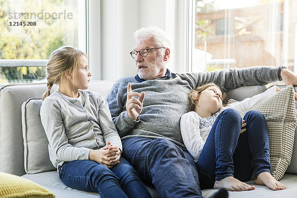 Großvater im Gespräch mit zwei Mädchen auf dem Sofa im Wohnzimmer