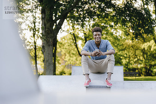 Lächelnder junger Mann mit Handy im Skatepark