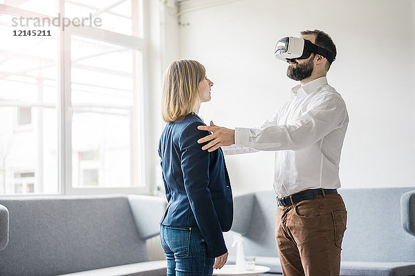 Geschäftsmann mit VR-Brille im Büro berührt Geschäftsfrau