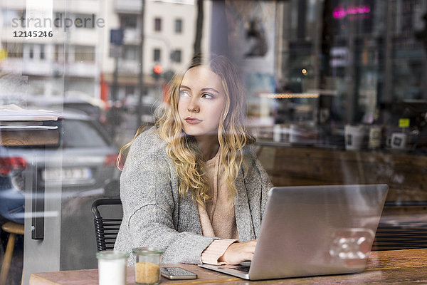 Porträt einer jungen Frau  die in einem Coffee-Shop am Laptop arbeitet