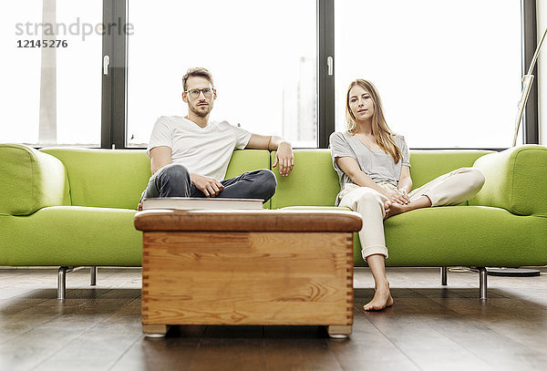 Porträt eines seriösen jungen Paares  das zu Hause auf der Couch sitzt.