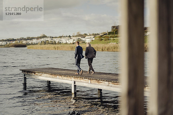 Zwei Geschäftsleute  die auf einem Steg am See spazieren gehen.