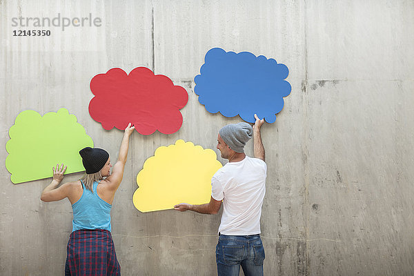 Mann und Frau befestigen bunte Wolkenformen an der Betonwand