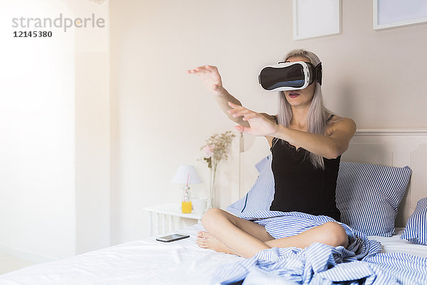 Junge Frau im Bett sitzend mit VR-Brille