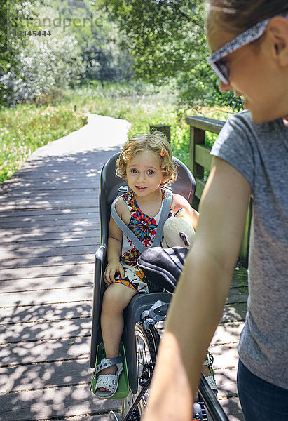 Kleines Mädchen sitzt mit seiner Mutter auf einem Kindersitz für Fahrräder.