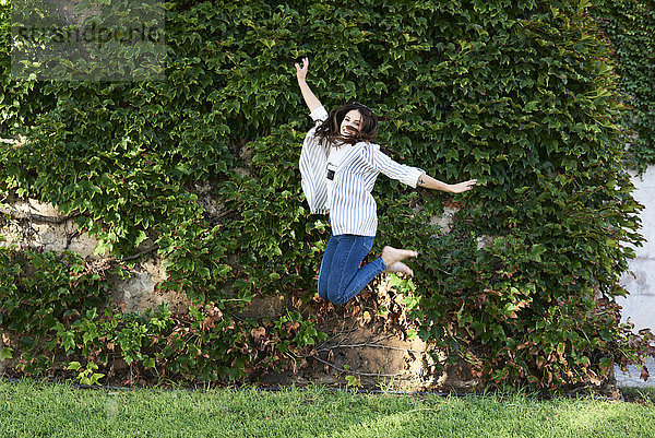 Fröhliche junge Frau  die im Freien in die Luft springt