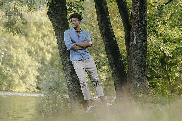 Junger Mann im Park lehnt an einem Baum am Wasser