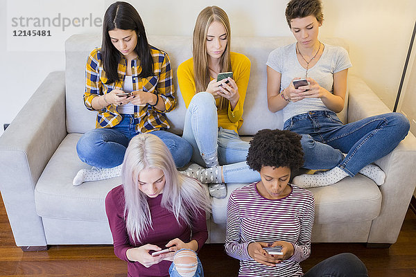 Gruppe von Freundinnen im Wohnzimmer besessen von ihren Smartphones
