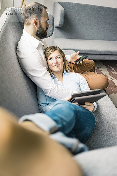 Lächelnde Frau mit Tablette und Mann mit Handy auf Couch