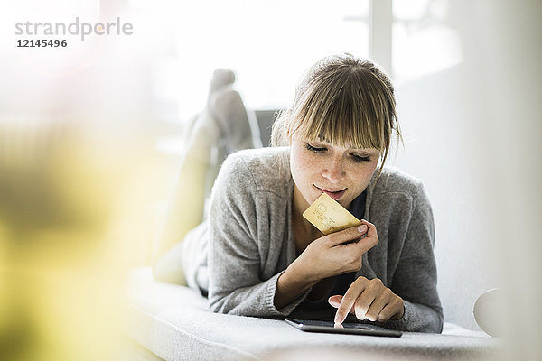 Frau auf der Couch liegend mit Kreditkarte und Tablett