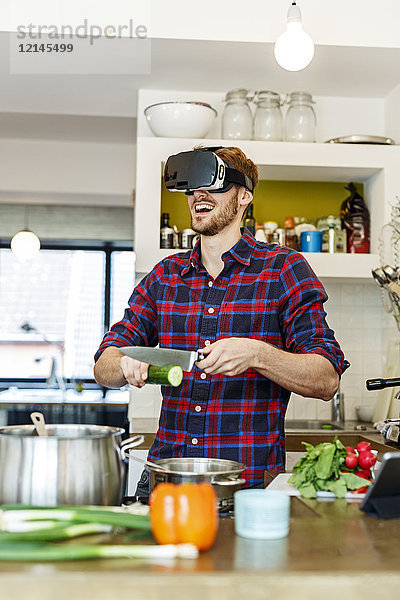 Glücklicher junger Mann mit VR-Brille beim Kochen in der Küche