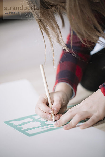 Mädchenhände trödeln mit Schablone und Bleistift