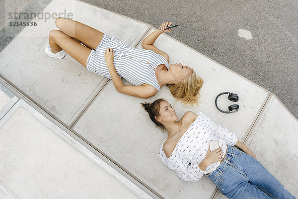 Zwei junge Frauen mit Handy und Kopfhörer im Skatepark