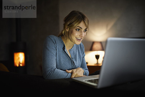 Porträt einer verblüfften Frau  die abends zu Hause mit dem Laptop unterwegs ist.