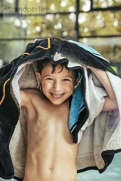Porträt eines glücklichen Jungen  der sich am Pool eines Hallenbades abtrocknet.
