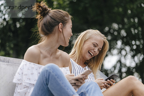 Zwei lachende junge Frauen mit Handys im Freien