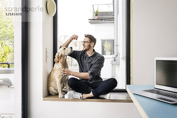 Glücklicher Mann mit Hund am Fenster sitzend
