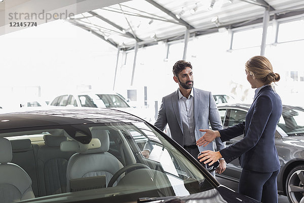 Autoverkäuferin zeigt Neuwagen dem männlichen Kunden im Autohaus-Showroom
