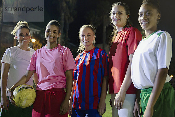 Portrait lächelnde  selbstbewusste junge Fußballerinnen mit Ball auf dem Spielfeld bei Nacht