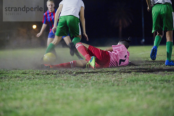 Junge Fußballspielerin fällt  tritt den Ball und spielt nachts auf dem Spielfeld.