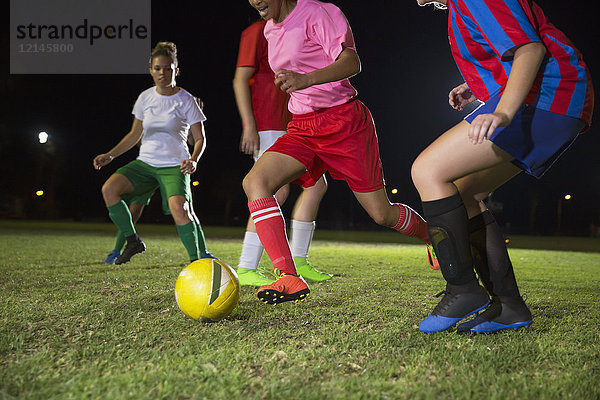 Junge Fußballspielerinnen  die nachts auf dem Spielfeld spielen und um den Ball rennen.