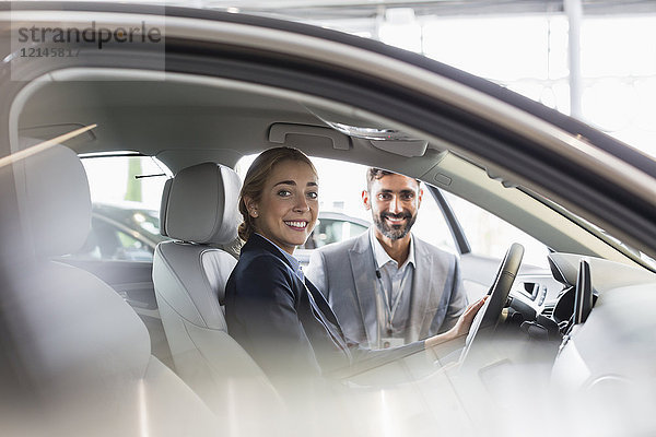 Porträt einer lächelnden Frau und eines Autoverkäufers im Neuwagen im Autohaus