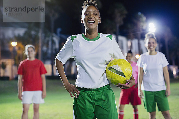 Portrait selbstbewusst  lachende junge Fußballspielerin  die nachts auf dem Spielfeld trainiert.