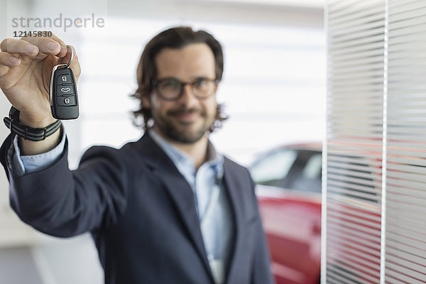 Porträt eines selbstbewussten Autoverkäufers  der den Autoschlüssel im Autohaus zeigt.