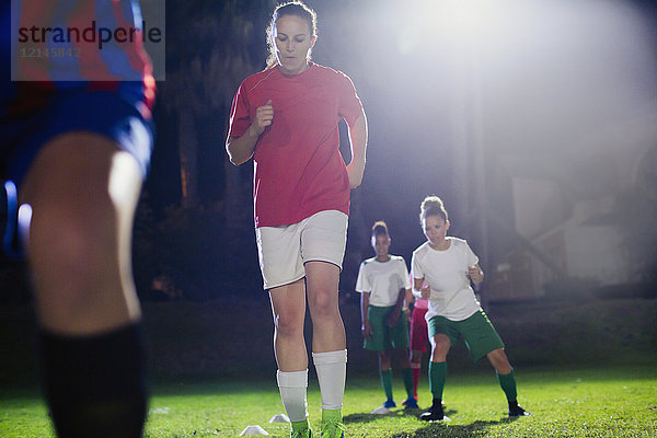 Junge Fußballspielerinnen üben nachts auf dem Spielfeld Agility-Sportübungen.