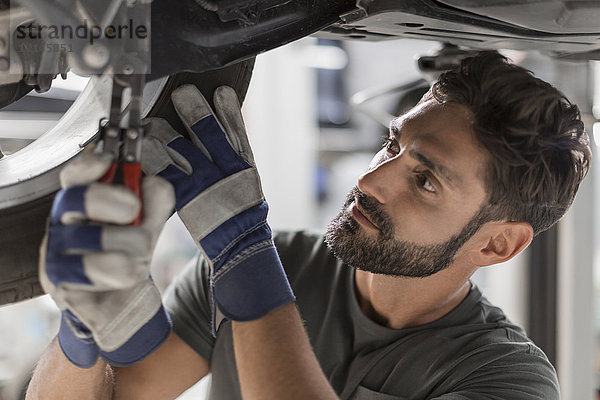 Fokussiertes männliches mechanisches Befestigungsrad unter dem Auto in der Werkstatt