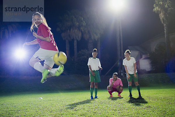 Junge Fußballspielerinnen  die nachts auf dem Spielfeld trainieren und den Rückstoß ausführen