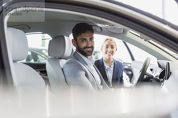 Portrait lächelnde  selbstbewusste Autoverkäuferin und männliche Kundin im Fahrerset des Neuwagens im Autohaus