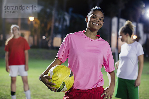Portrait selbstbewusste  lächelnde junge Fußballspielerin mit Ball auf dem Spielfeld bei Nacht