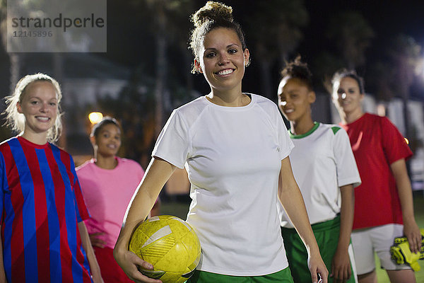 Portrait lächelndes  selbstbewusstes junges weibliches Fußballteam mit Ball auf dem Spielfeld bei Nacht