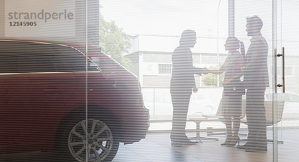 Autoverkäufer beim Händeschütteln mit ein paar Kunden im Autohaus-Showroom