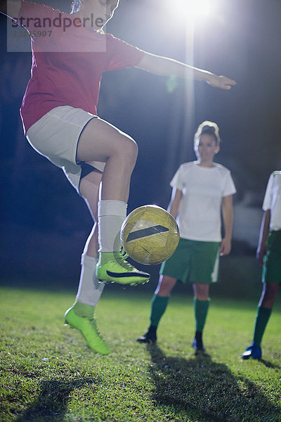 Junge Fußballspielerin übt  springt und tritt den Ball nachts auf dem Spielfeld.