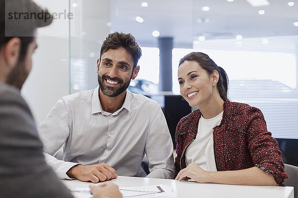 Lächelndes Paar Kunden im Gespräch mit Autoverkäufer im Autohausbüro