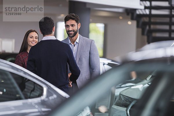 Autoverkäufer-Gruß  Händeschütteln mit ein paar Kunden im Autohaus-Showroom