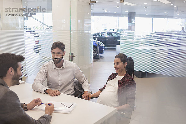 Autoverkäufer im Gespräch mit einem schwangeren Paar im Autohausbüro