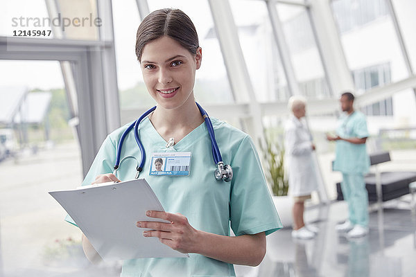 Portrait lächelnde  selbstbewusste Krankenschwester mit Klemmbrett im Krankenhaus