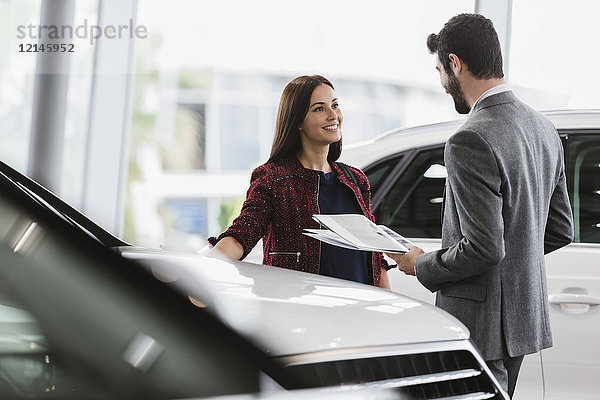 Autoverkäuferin zeigt dem männlichen Kunden im Autohaus die Broschüre