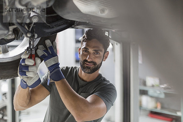 Portrait zuversichtlich männlich Kfz-Mechaniker arbeiten unter dem Auto in der Kfz-Werkstatt