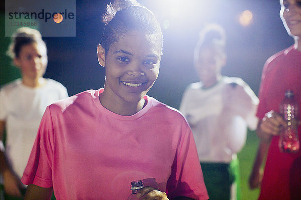Portrait selbstbewusste junge Fußballspielerin auf dem Spielfeld mit Mannschaftskameraden bei Nacht