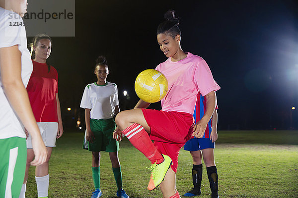 Junge Fußballspielerin beim Üben  nachts Ball auf dem Knie auf dem Feld hüpfend