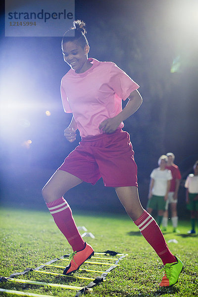 Junge Fußballspielerinnen üben nachts auf dem Spielfeld Agility-Sportübungen.